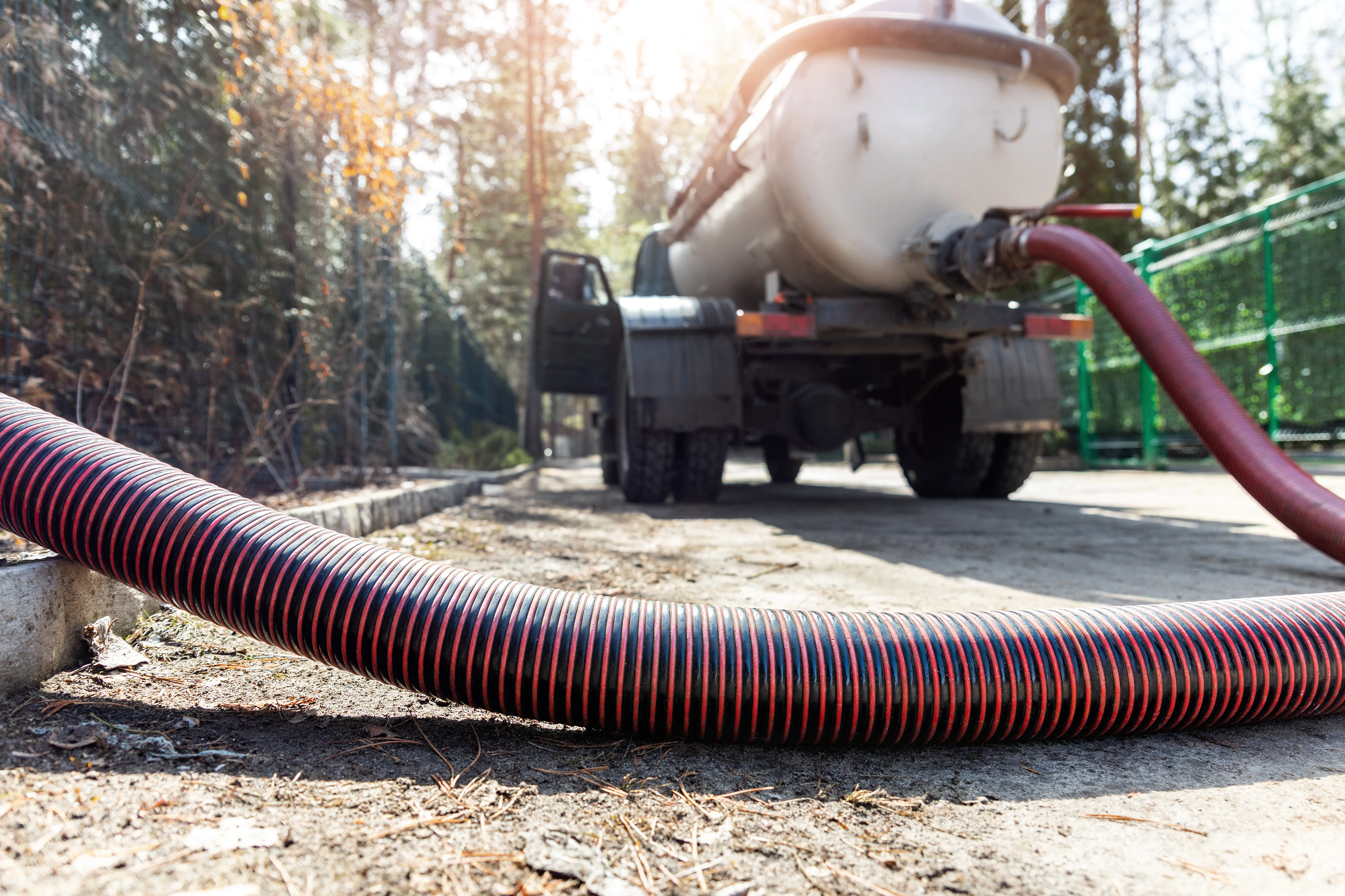 The red and black hose from the septic tank truck stretches along the ground and continues off frame.